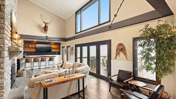 A spacious living area with a fireplace, a sofa, a dining table, and a large window overlooking a deck. - Luxury VIEWS from 4700', Hot Tub, Modern Rustic (Seven Devils)