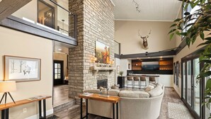 A spacious living area with a fireplace, a large sofa, and a dining area with bar stools. - Luxury VIEWS from 4700', Hot Tub, Modern Rustic (Seven Devils)