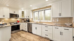 A modern kitchen with white cabinetry, stainless steel appliances, and a large window providing natural light. - Luxury VIEWS from 4700', Hot Tub, Modern Rustic (Seven Devils)