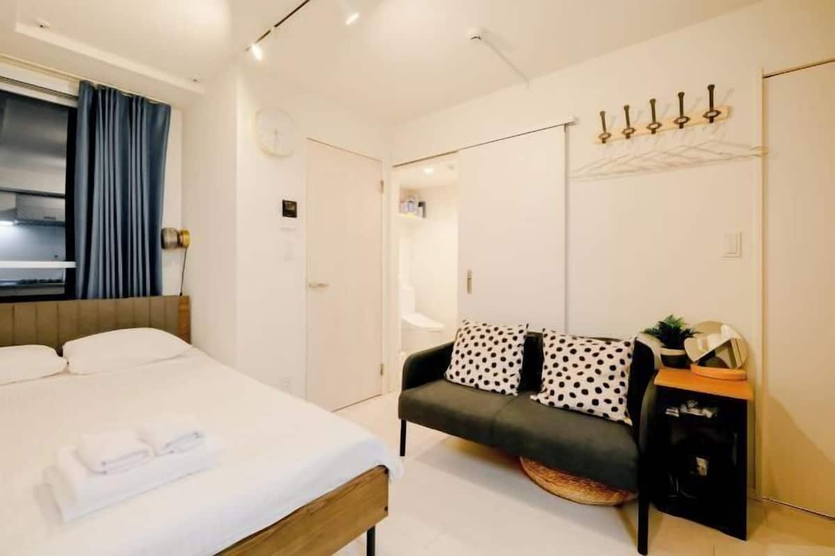 A modern hotel room with a bed, a sofa, a small table, and a coat rack.