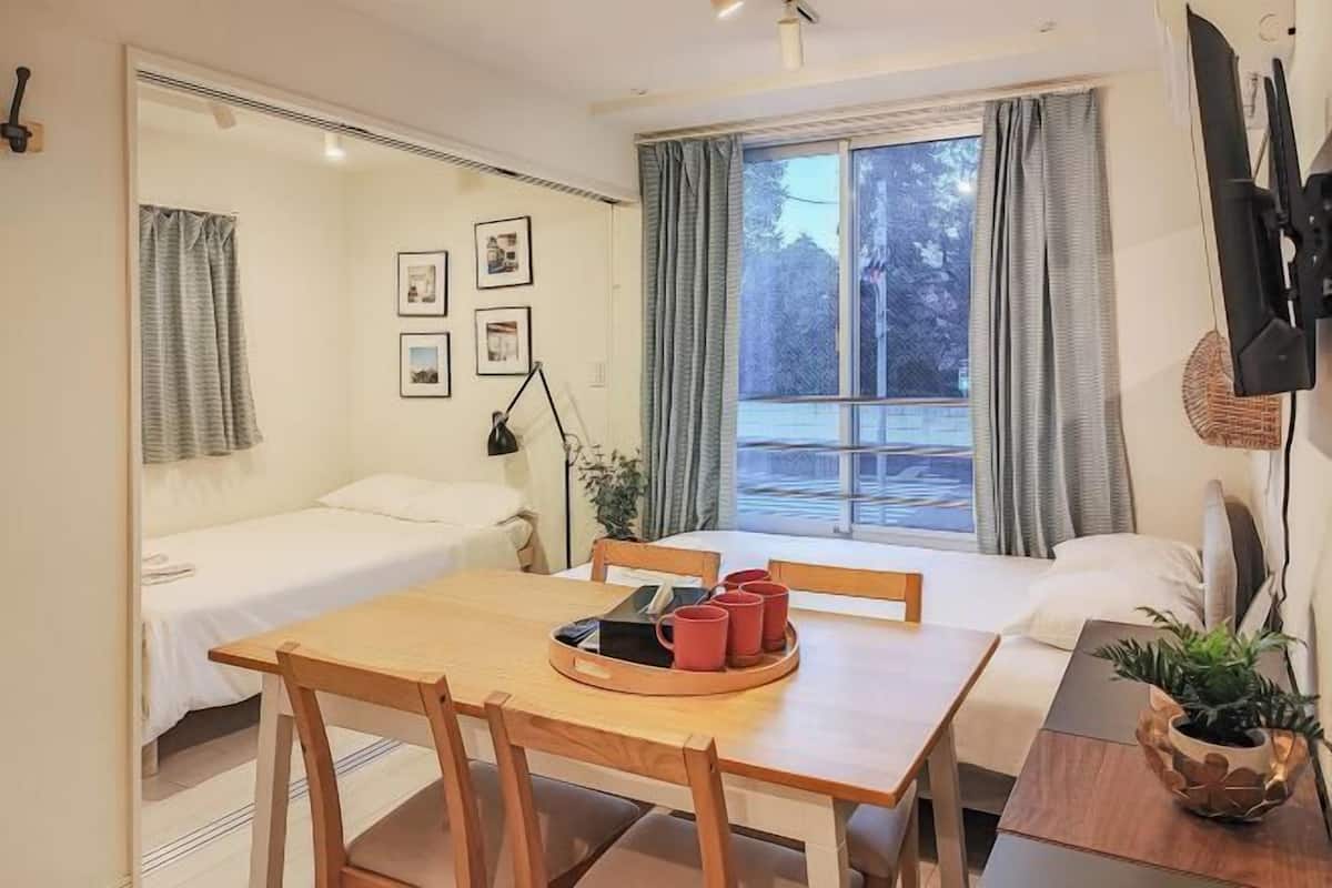 A room with a bed, a small table with a tray of red cups, a chair, and a potted plant.