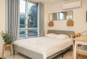 A bedroom with a bed, a dining table, a chair, a potted plant, a window with curtains, and a wall-mounted air conditioner. - Mi-HOTEL KAGURA (Tokyo)