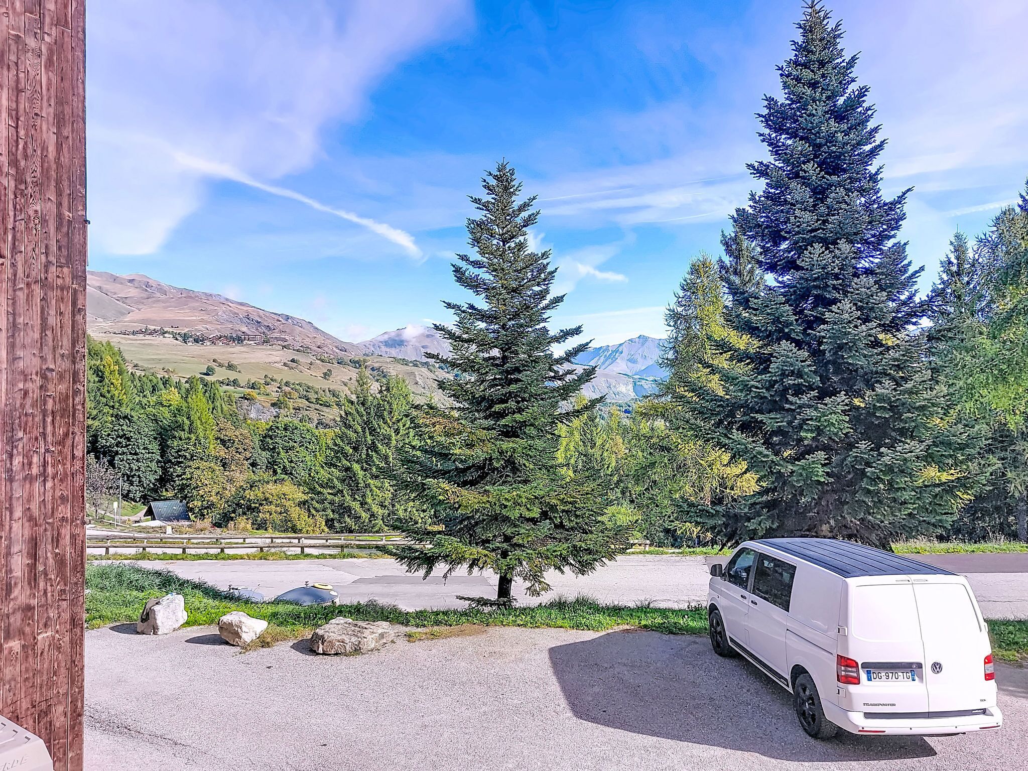 Uma van branca estacionada em uma entrada de cascalho, com paisagem de montanhas ao fundo.