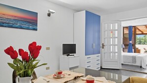 Een moderne kamer met een flatscreen televisie, een eettafel met een vaas rode tulpen, een witte karaf en een blauwe garderobe.