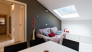 A modern living room with a skylight, a sofa with patterned cushions, a dining table with chairs, and a small side table with decorative items.