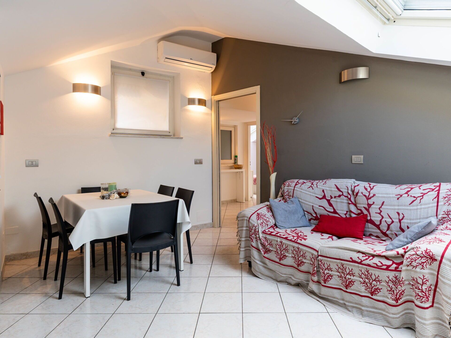 A dining area with a table and chairs, a sofa with a patterned cover, and a ceiling light.