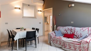 A dining area with a table and chairs, a sofa with a patterned cover, and a ceiling light.
