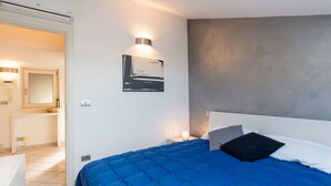 A modern bedroom with a large bed, a nightstand, a wall-mounted light, and a bathroom visible through an open door.