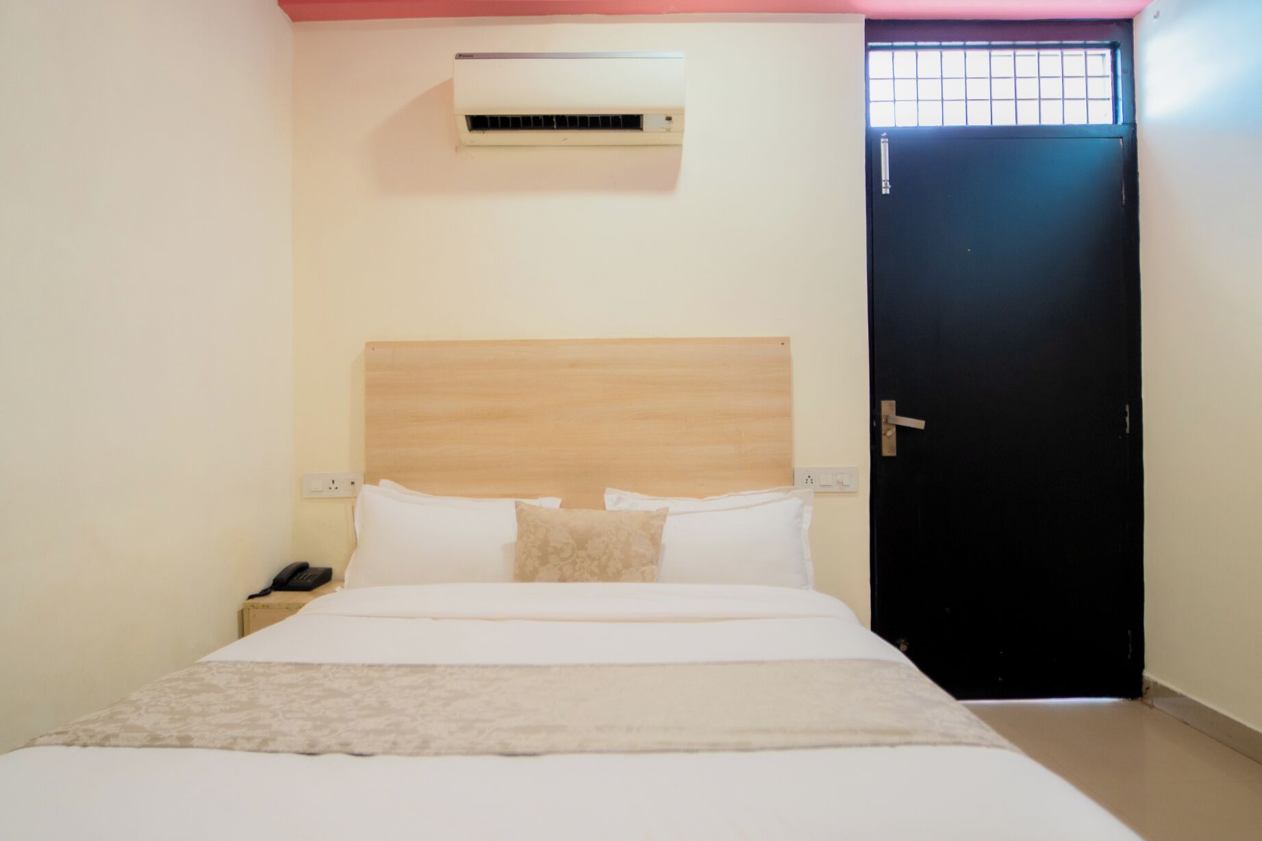 Un dormitorio con cama, mesita de noche, unidad de aire acondicionado y una puerta.