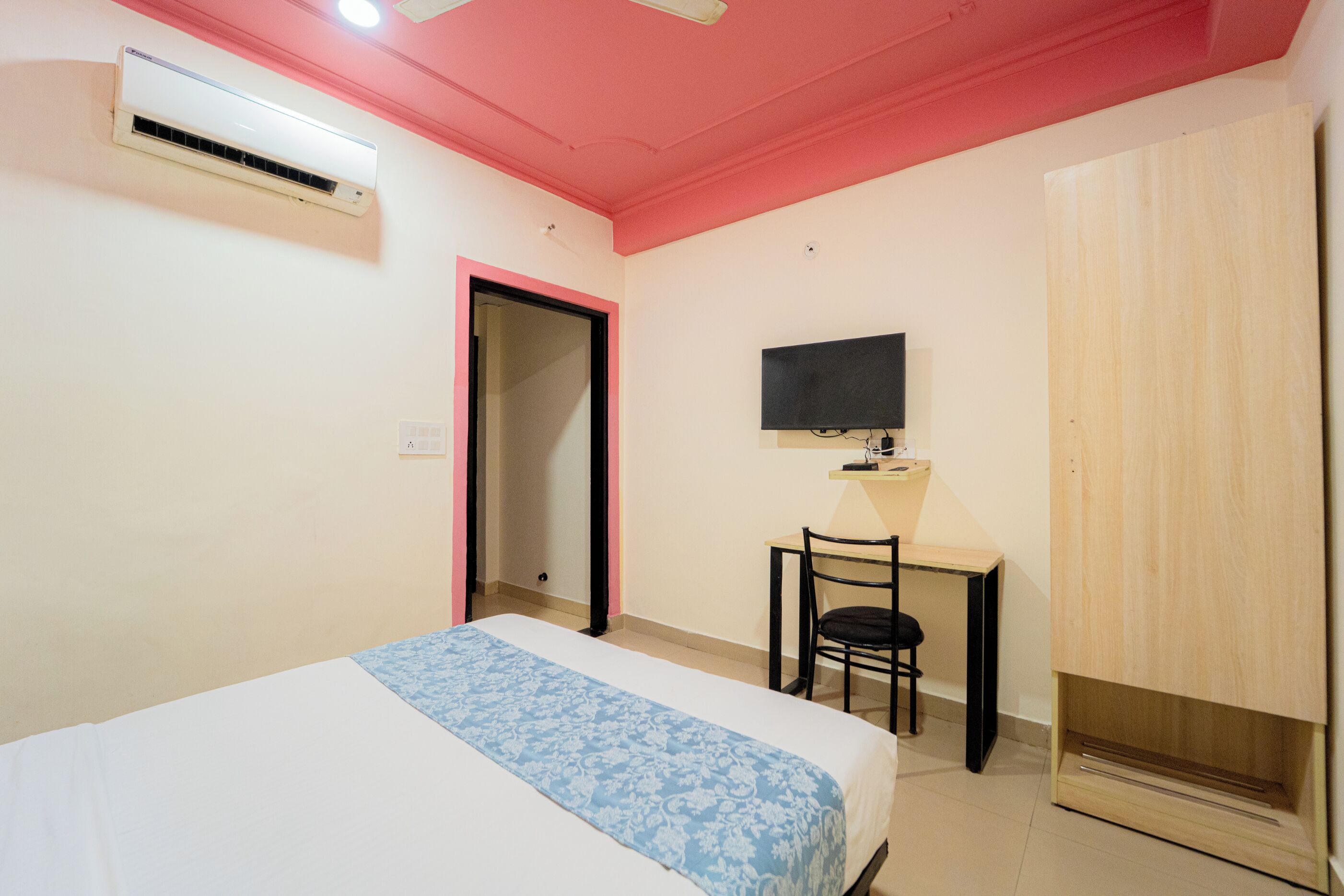 Un dormitorio con cama, escritorio, silla, televisor y aire acondicionado.