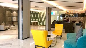 A hotel lobby with a reception desk, seating area with yellow chairs, a teal sofa, and a marble floor. - Joy Hotel (Phnom Penh)