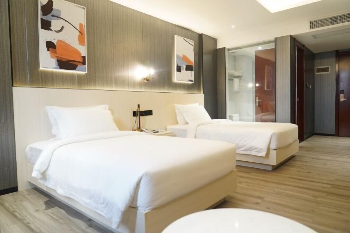 A hotel room with two beds, a large mirror, and a wooden floor.