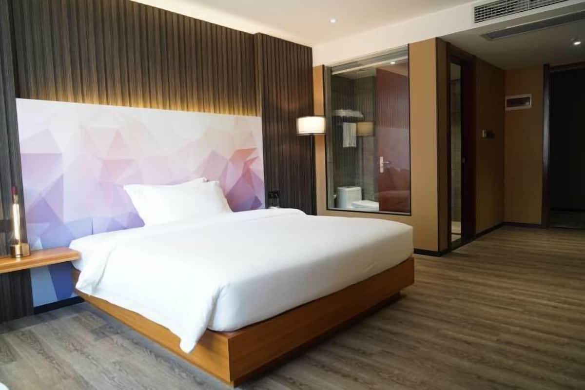 Une chambre d’hôtel moderne avec un lit en bois, une table de chevet, une tête de lit à motifs géométriques, une cabine de douche en verre et un plancher en bois.