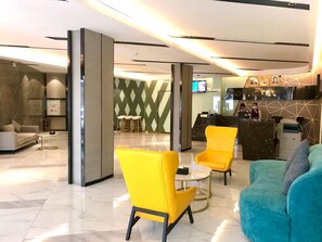 A hotel lobby with a reception desk, seating area with yellow chairs, a teal sofa, and a marble floor. - Joy Hotel (Phnom Penh)