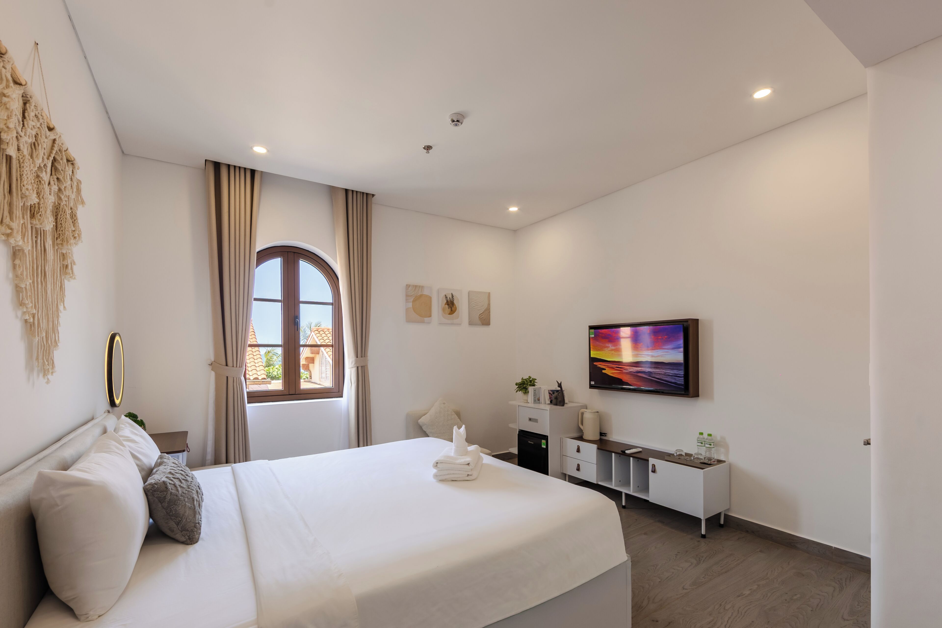 A modern hotel room with a large bed, a desk, a chair, a TV, and a window with curtains.