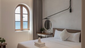 A hotel room with a large bed, a bedside table with a mirror, a small desk, a window with curtains, and a view of the sea. - Lucie Cozy Home - Sunset Town Phu Quoc (Phu Quoc)
