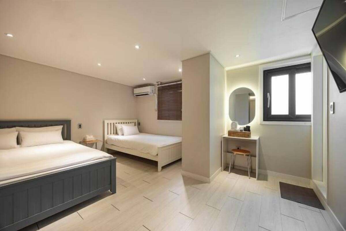 A bedroom with a large bed, a smaller bed, a desk with a chair, a mirror, and a television.