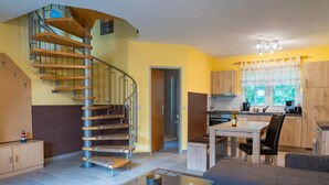 A modern kitchen with a built-in oven, a dining table with chairs, and a spiral staircase leading to an upper level. - Am Deich Haus 32 - Comfortable vacation home on the dike with terrace, garden and (Zingst)