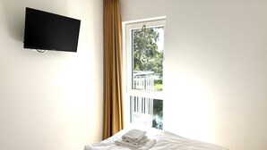 Una habitación de hotel con cama, televisor montado en la pared y ventana con cortinas.