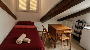 Ein kleiner, gemütlicher Raum mit einem Bett, einem Holztisch mit Stühlen, einem kleinen Kühlschrank und einem Fenster mit Jalousien.