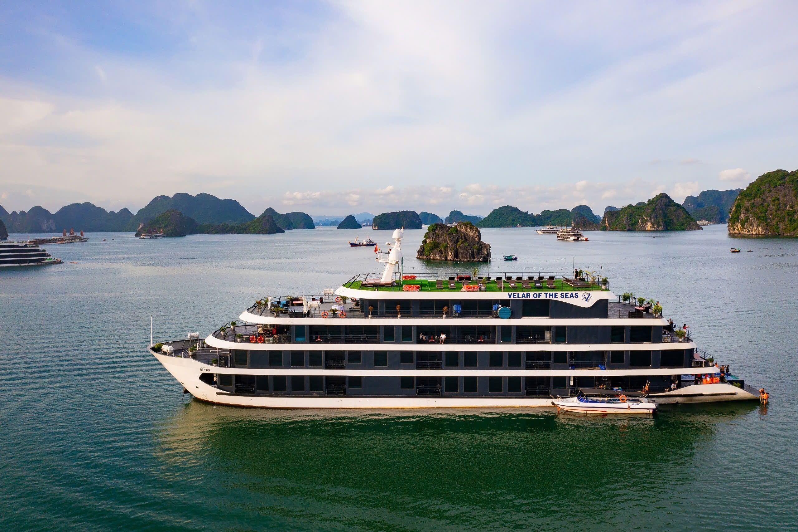 A large, multi-deck cruise ship with a prominent 'Velar of the Seas' sign, surrounded by calm waters and distant islands.