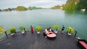 A boat deck with seating, potted plants, and a view of the water and greenery. - Velar Of The Sea Cruise (Tuan Chau)