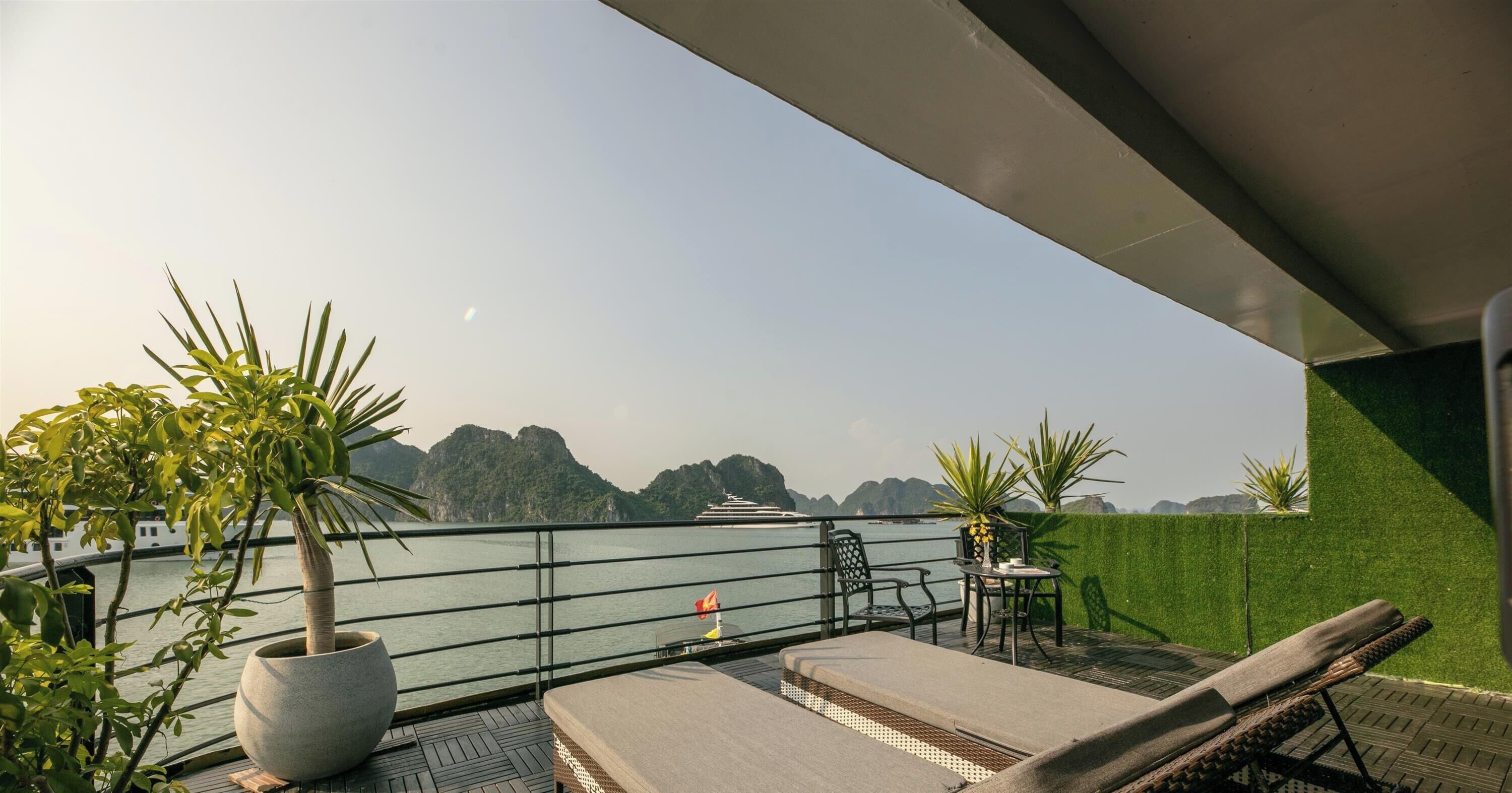 A balcony with lounge chairs, a potted plant, and a view of the sea and mountains.