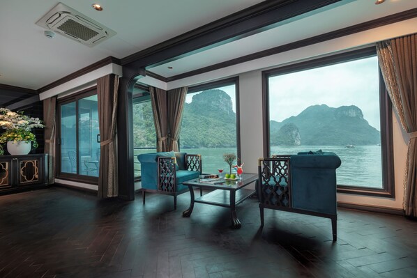 A spacious room with large windows overlooking a body of water and a mountainous landscape. There are two sofas and a coffee table with decorative items. - Velar Of The Sea Cruise (Tuan Chau)