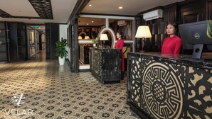 Una hall d'albergo con una reception, una pianta in vaso e una parete decorativa.