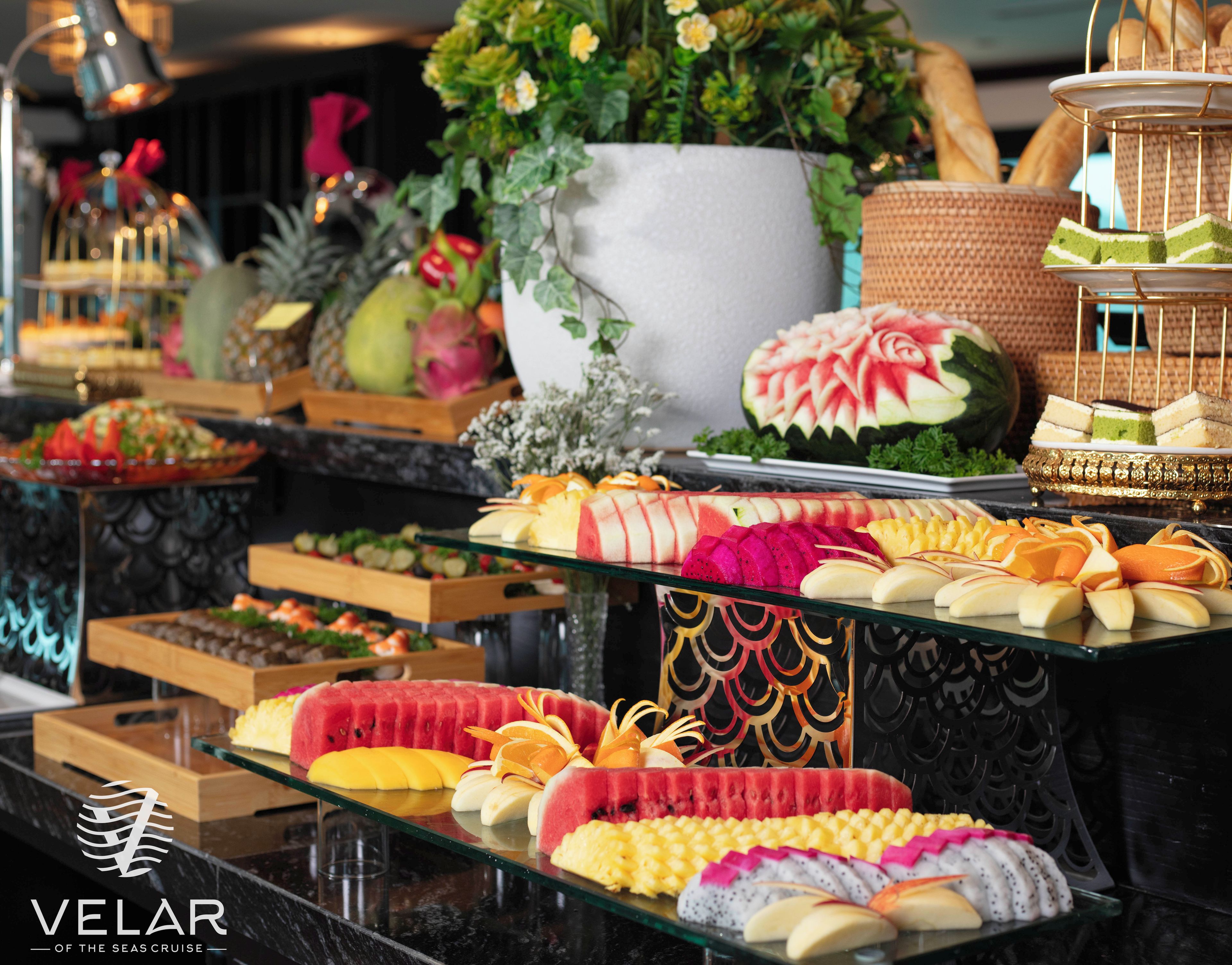 Buffet com diversos tipos de comida e uma placa indicando 'VELAR OF THE SEAS CRUISE'.