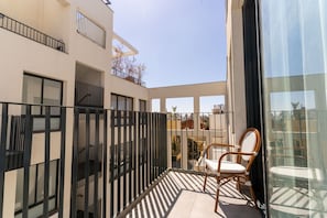 En balkon med en stol, en glasdør og udsigt til bygninger.