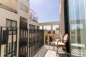 Ein Balkon mit einem Stuhl, einer Glastür und Blick auf Gebäude.