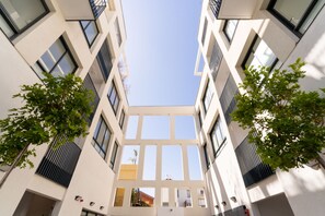 A modern building with a central atrium, large windows, and symmetrical design. - Luxury 3 rooms Apt• Balcony• Parking | HaKerem A45 (680012)