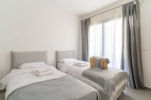 A room with two beds, a window with curtains, and a basket with towels. - Luxury 3 rooms Apt• Balcony• Parking | HaKerem A55 (680012)
