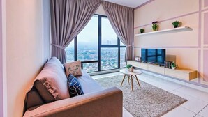 A modern living room with a sofa, a TV, a small coffee table, and a view of a cityscape through large windows. - Mid Valley Southkey Mosaic by RR JBcity (Plentong)