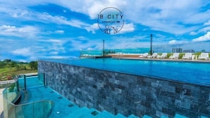 A pool with a glass barrier, a clear blue sky, and a logo for JB City Homestay Resort. - Mid Valley Southkey Mosaic by RR JBcity (Plentong)