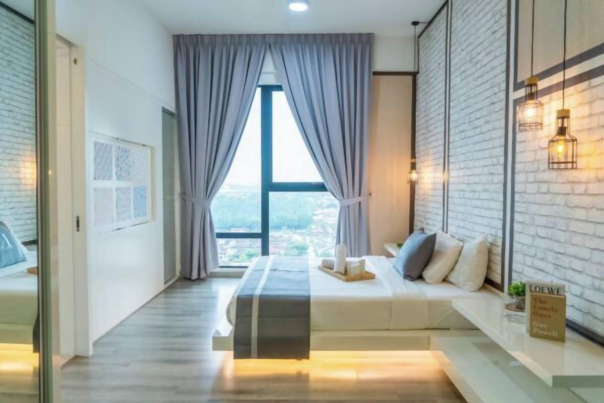 Een moderne hotelkamer met een groot raam, een bed met een bankje, een bakstenen muur en een bord aan de muur.