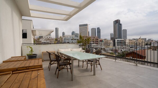 Une terrasse sur le toit avec une table et des chaises en verre, un banc en bois et une vue panoramique sur la ville.