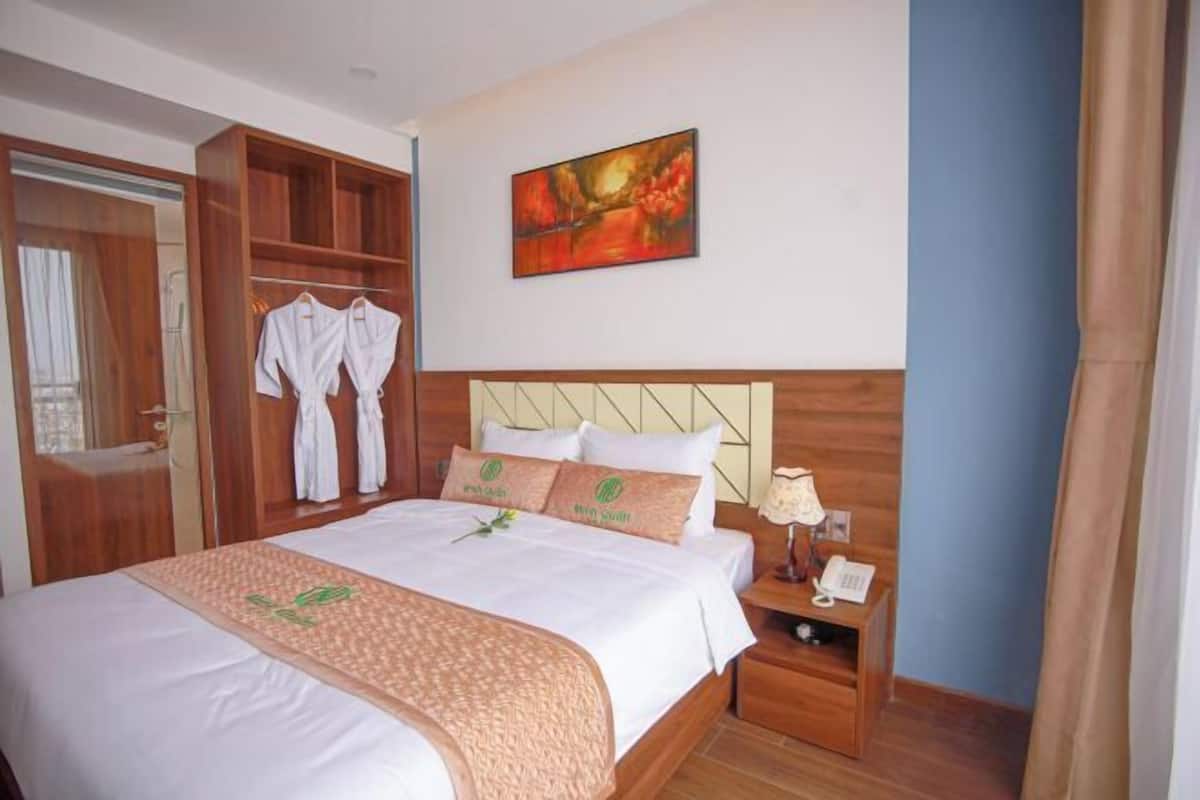 Habitación de hotel con una cama grande, cabecera de madera, un cuadro en la pared y un armario con batas.