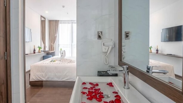 A modern hotel room with a large bed, a bathroom with a bathtub, and a large mirror. - Minh Quan Hotel - Da Nang Center by Hos (Da Nang)