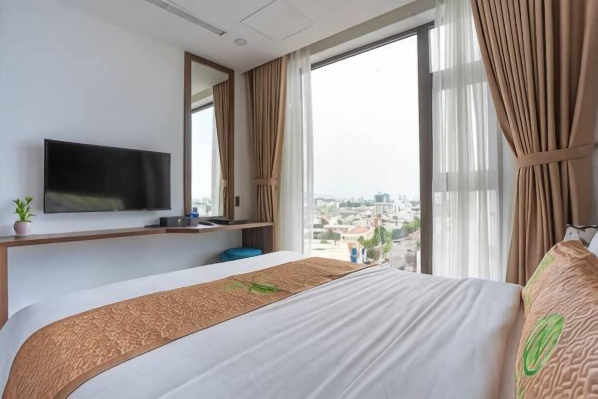 A hotel room with a bed, a TV, a window with curtains, and a view of the city.