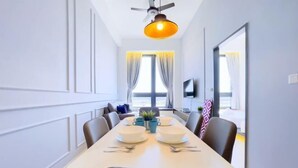 Een eethoek met een lange tafel gedekt voor vier personen, een plafondventilator en een aan de muur bevestigde televisie.