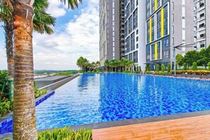 A swimming pool with a wooden deck, surrounded by tall residential buildings with balconies. - Sunway Grid by RR JBcity (Iskandar Puteri)