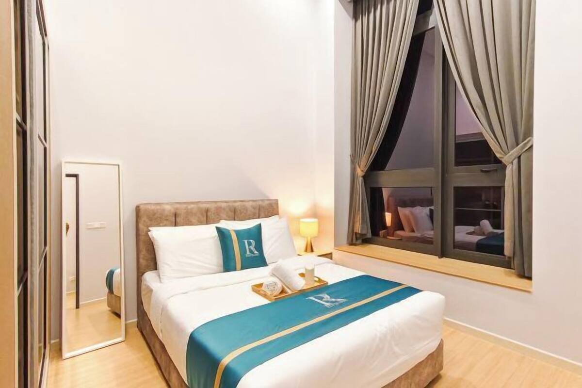 Een hotelkamer met een bed, nachtkastje, raam met gordijnen en een deur.