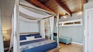 Ein Himmelsbett mit blau-weißer Bettdecke, einem Holz-Kopfteil und einem Nachttisch mit Lampe.