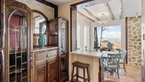 Ein Zimmer mit einem Holzschrank, einem kleinen Hocker und einem Tisch mit Stühlen. Ein Durchgang bietet Blick ins Freie.