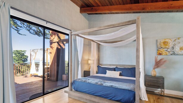 Ein Schlafzimmer mit Himmelbett, Holzboden, Nachttisch mit Lampe und Blick auf eine Terrasse.