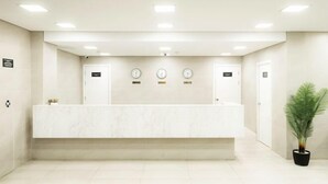 A reception area with a marble counter, clocks, and a potted plant. - Highvill Hotel (Astana)