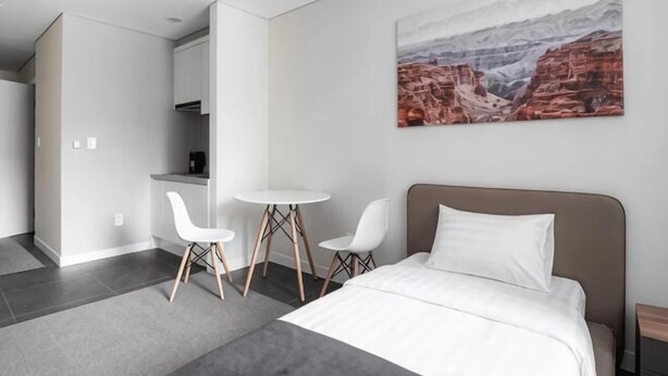A modern hotel room with a bed, two white chairs, a small table, and a painting of a canyon on the wall. - Highvill Hotel (Astana)