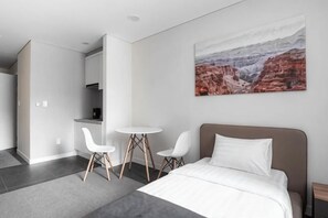 A modern hotel room with a bed, two white chairs, a small table, and a painting of a canyon on the wall. - Highvill Hotel (Astana)